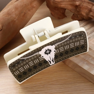 Detail of a cream hair claw clip with olive green geometric patterns and a white bull skull
