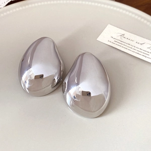 Polished silver irregular teardrop earrings placed on an elegant ceramic tray