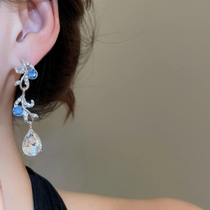 Detail of silver drop earrings with blue and clear gems worn by a model