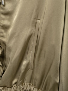Detail of khaki green satin jacket featuring a welt pocket and adjustable drawstring hem