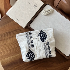 Close-up of white linen cosmetic bag with blue embroidery and lace trim on wood surface