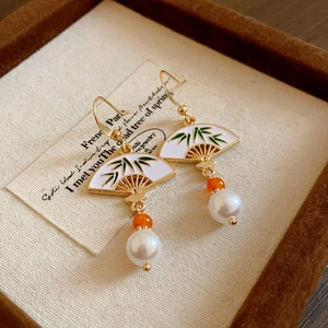 Detail of fan-shaped golden earrings with green bamboo leaf motif and dangling pearls