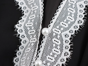 Detail of elegant V-neck with white lace trim and decorative pearl buttons on black fabric