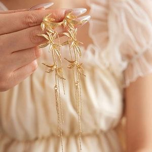 Detail of gold bamboo leaf earrings with long tassels held against a soft fabric background