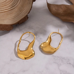 Golden irregular earrings with liquid metal texture on white marble and wood background