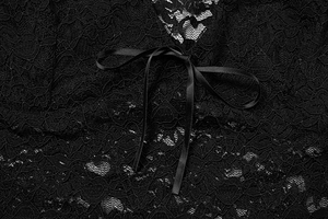 Macro detail of elegant black floral lace fabric with a delicate silk ribbon bow accent