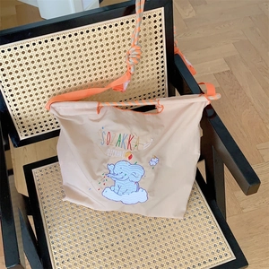 Detail of cute elephant embroidery on beige tote bag with bright orange nylon shoulder strap