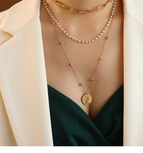Detail of layered gold titanium steel necklaces with pearls and a queen coin pendant