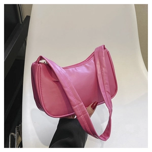 Pink crescent hobo bag with a wide shoulder strap held against a minimalist white chair