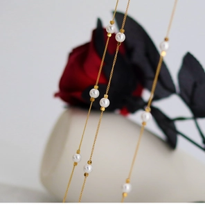 Close-up of gold chain necklace with five white round pearls and elegant rose backdrop