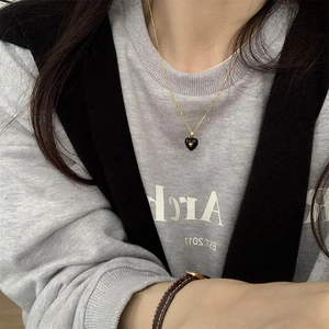 Close-up of a French retro gold chain necklace featuring a black heart enamel pendant