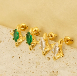 Macro view of gold studs with emerald and white marquise-cut stones on stone base
