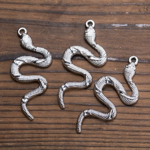 Three vintage silver snake-shaped alloy pendants on a rustic brown wood background