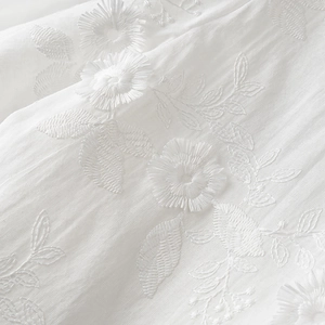 Detailed macro view of delicate white floral embroidery on premium cotton fabric