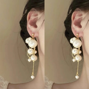 Detail of layered white pearl drop earrings with golden chains on a model