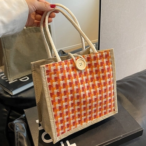 Hand holding a beige jute woven handbag with colorful pattern and rope handle