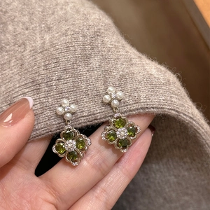 Detailed shot of golden flower earrings with green zircon and pearls held by hand