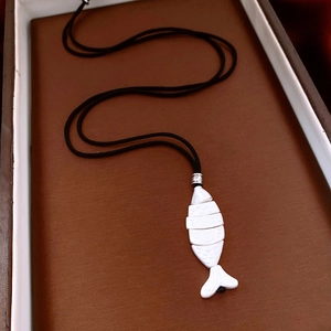 Artistic white articulated fish pendant with black cord on textured brown background