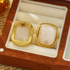 Macro shot of 18k gold square earrings with white marble texture on velvet tray