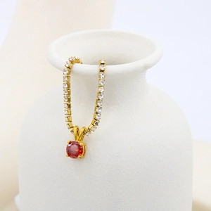 Detailed close-up of a gold birthstone pendant necklace with red zircon and crystal accents