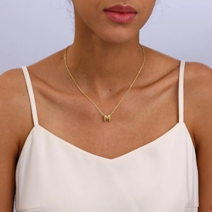 Detail of 18K gold plated bubble letter M pendant necklace on female model