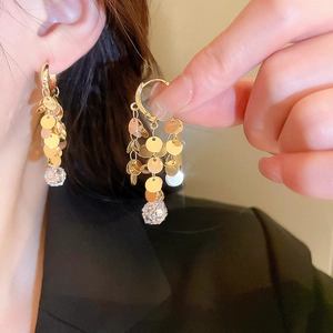 Macro detail of gold tassel earrings with leaf sequins and faceted crystal pendant