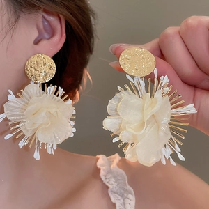 Detailed view of cream fabric flower earrings with textured gold metal and tassels