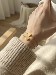 Close-up of minimalist heart charm bracelets in 18k gold finish worn on a wrist