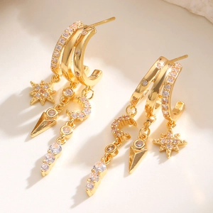Detail of layered gold earrings featuring star, moon and zircon drop charms on rings