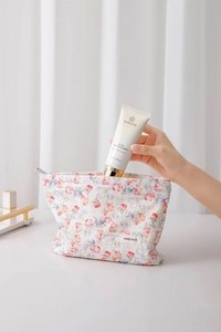 Close-up of hand putting cream into a floral jacquard cotton makeup bag with zipper