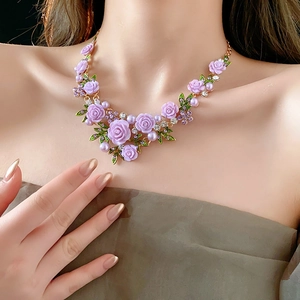 Gros plan d'un collier floral avec roses en résine violette, feuilles et perles sur modèle