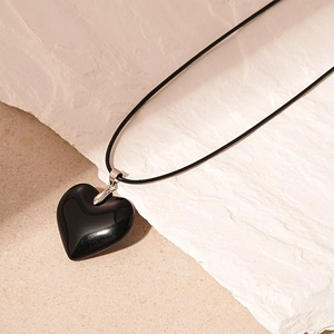 Macro detail of a heart-shaped obsidian pendant with shiny silver metal clasp and cord