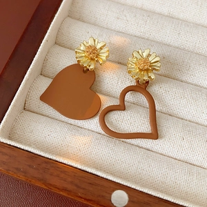 Detailed close-up of asymmetrical heart earrings with golden daisies in a jewelry box