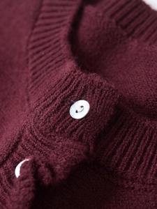 Macro shot of burgundy knitted cardigan with white shell buttons and ribbed edge detail