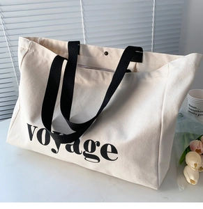 Minimalist beige canvas tote bag with black voyage lettering shown in a lifestyle setting