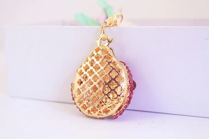 Makroaufnahme eines goldenen Tropfenanhängers mit rosa Steinen und Metallclip