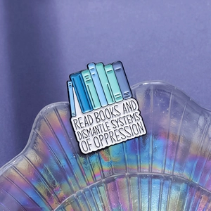 Stack of books enamel pin featuring the phrase READ BOOKS AND DISMANTLE SYSTEMS OF OPPRESSION