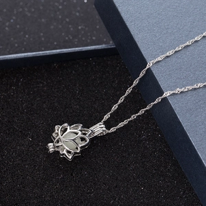 Detailed view of silver lotus locket necklace with glow bead on dark jewelry padding