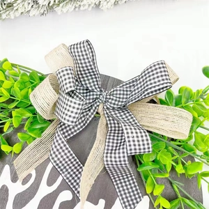 Detail of buffalo plaid bow and lush faux greenery on a round wooden welcome door sign