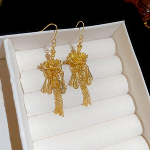 Makroaufnahme von goldenen Lotus-Quasten-Ohrringen auf einer beigen Schmuckschatulle