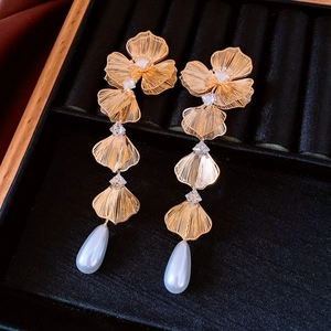 Dettaglio ravvicinato di orecchini a fiore dorati con zirconi e perle bianche pendenti