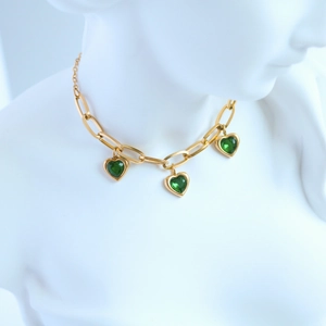 Close-up of gold paperclip chain necklace with three heart-shaped green gemstones