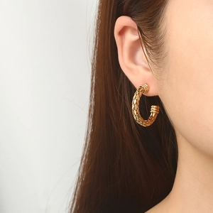 Gros plan de boucles d'oreilles C dorées avec texture tressée sur un mannequin