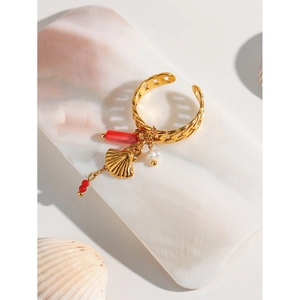 Detail of gold open ring with red bead, pearl and shell pendants on a nacre background