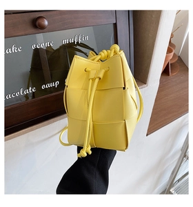 Detail of yellow woven leather bucket bag with drawstring closure held by a model