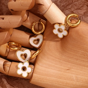 Detail of 18K gold earrings with white hollow heart and flower charms on a hand model