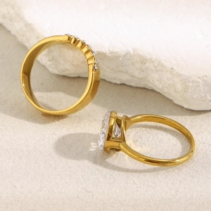 Detail of two 18K gold plated rings with oval zircons on a white textured rock