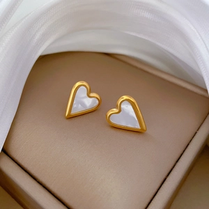 Close-up of heart-shaped gold studs with white shell inlay on elegant silk fabric