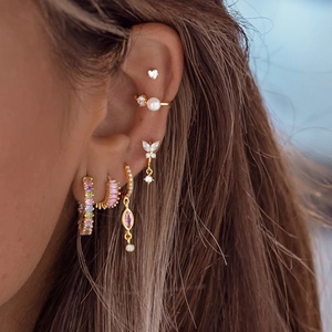 Close-up of model wearing gold earrings set with pearls, zircons, and butterfly charms