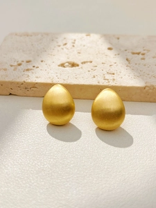 Detailed view of teardrop earrings with a matte brushed gold finish on travertine stone